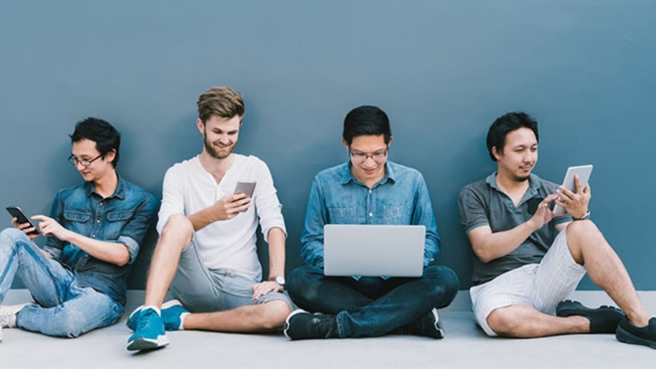 A group of four young people sat around using multiple devices