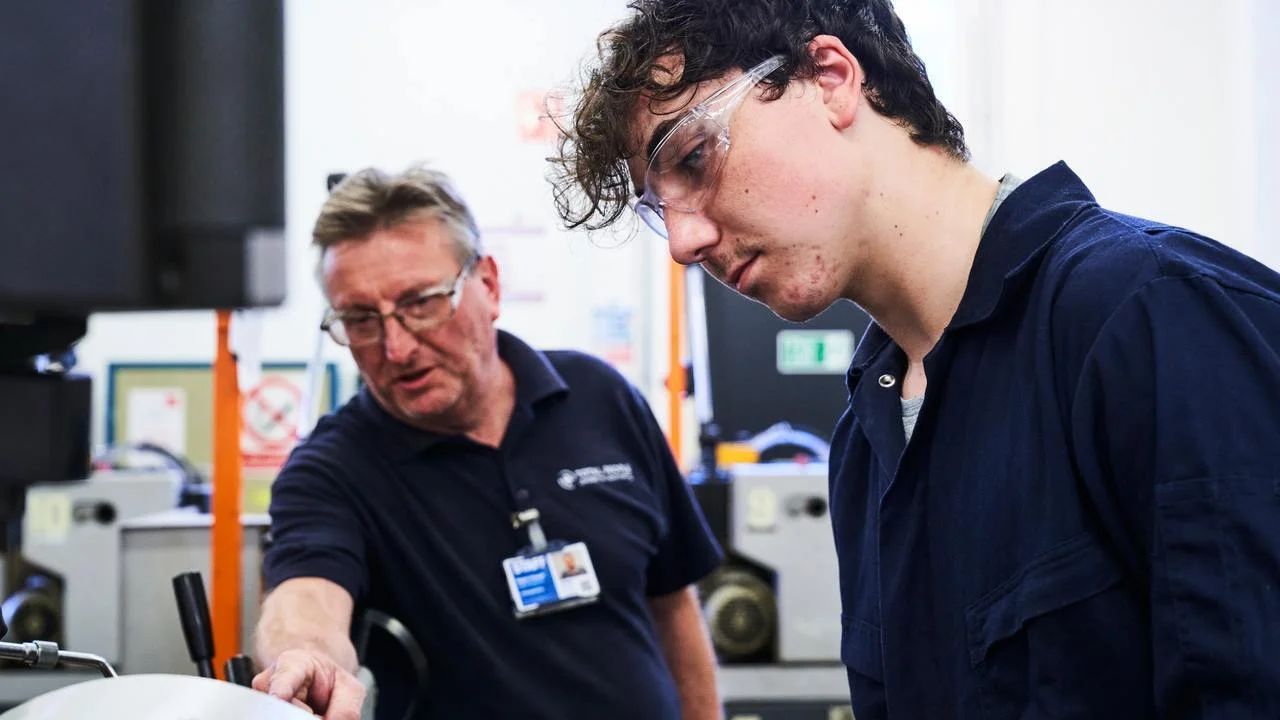 Engineering student receiving hands-on instruction from a tutor while operating machinery in a workshop