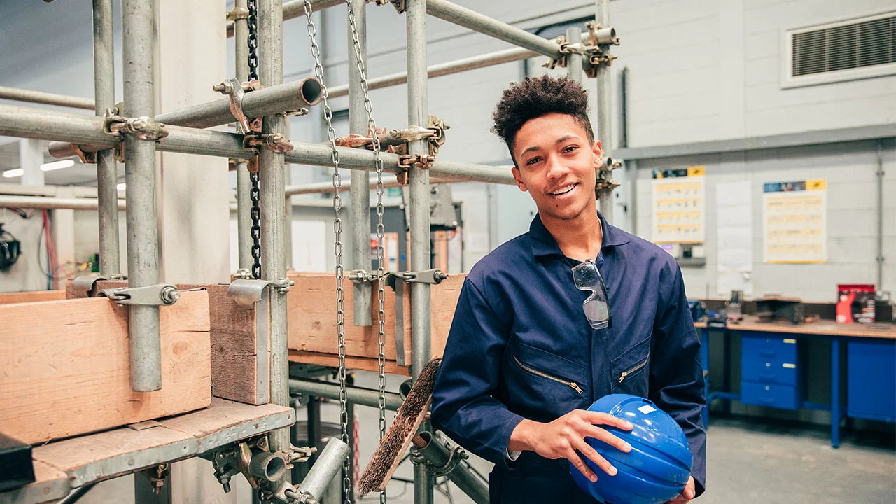 An apprentice smiling in front of some scaffolding