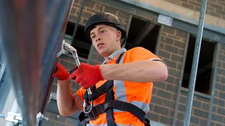 Person wearing a hard hat, high-visibility clothing and safety harness working on a construction site.