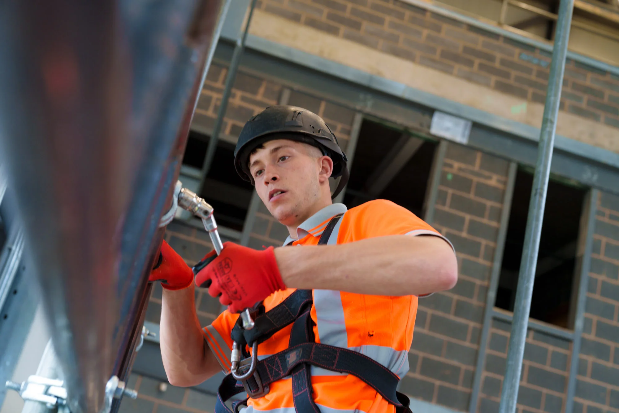 Person wearing a hard hat, high-visibility clothing and safety harness working on a construction site.