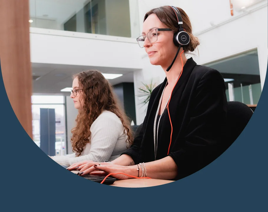 Person wearing a headset and using a computer at a desk in a modern office environment.