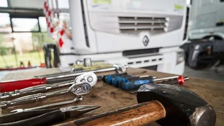 In the foreground there are some tools on a table including a large hammer. In the background, slightly out of focus, is the cab of a lorry.