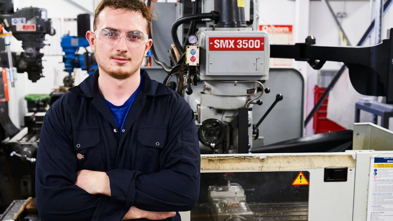 Engineering student standing in a workshop with industrial machinery used for practical engineering training