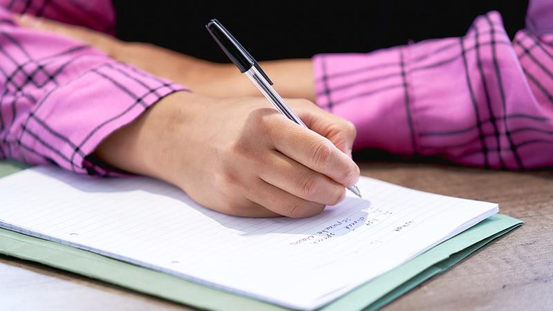 Person writing notes on apprenticeship paperwork in a notebook, completing training or contract documentation.
