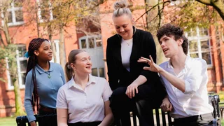Group of apprentices and colleagues sitting and standing outdoors near office buildings, talking together.