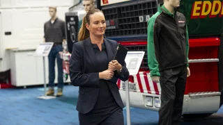 Female apprentice walking with clipboard in front of HGV.