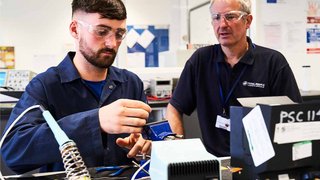 An engineering apprentice is working while being supervised by his tutor.