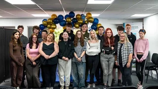 17 Study Programme learners stand together in front of a blue and gold balloon arch after being recognised at the Study Programme Awards.