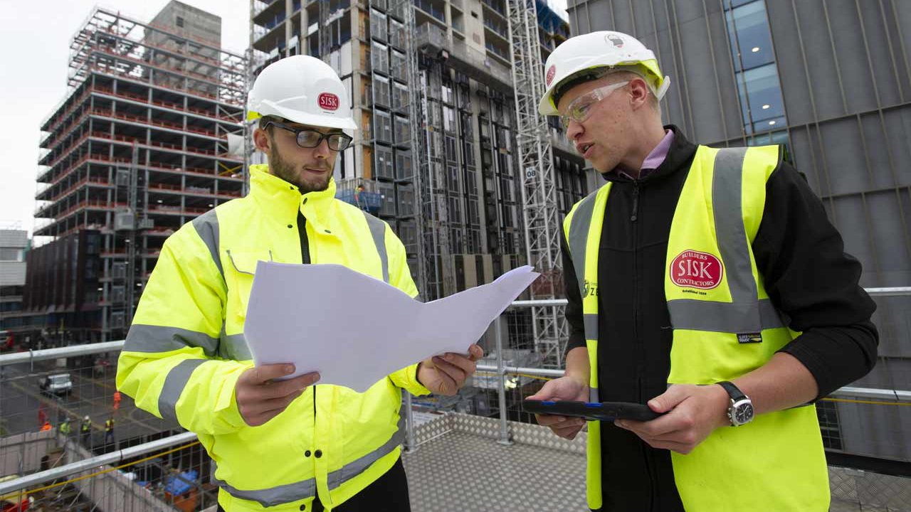 Two male apprentices in hard hats on a building site.