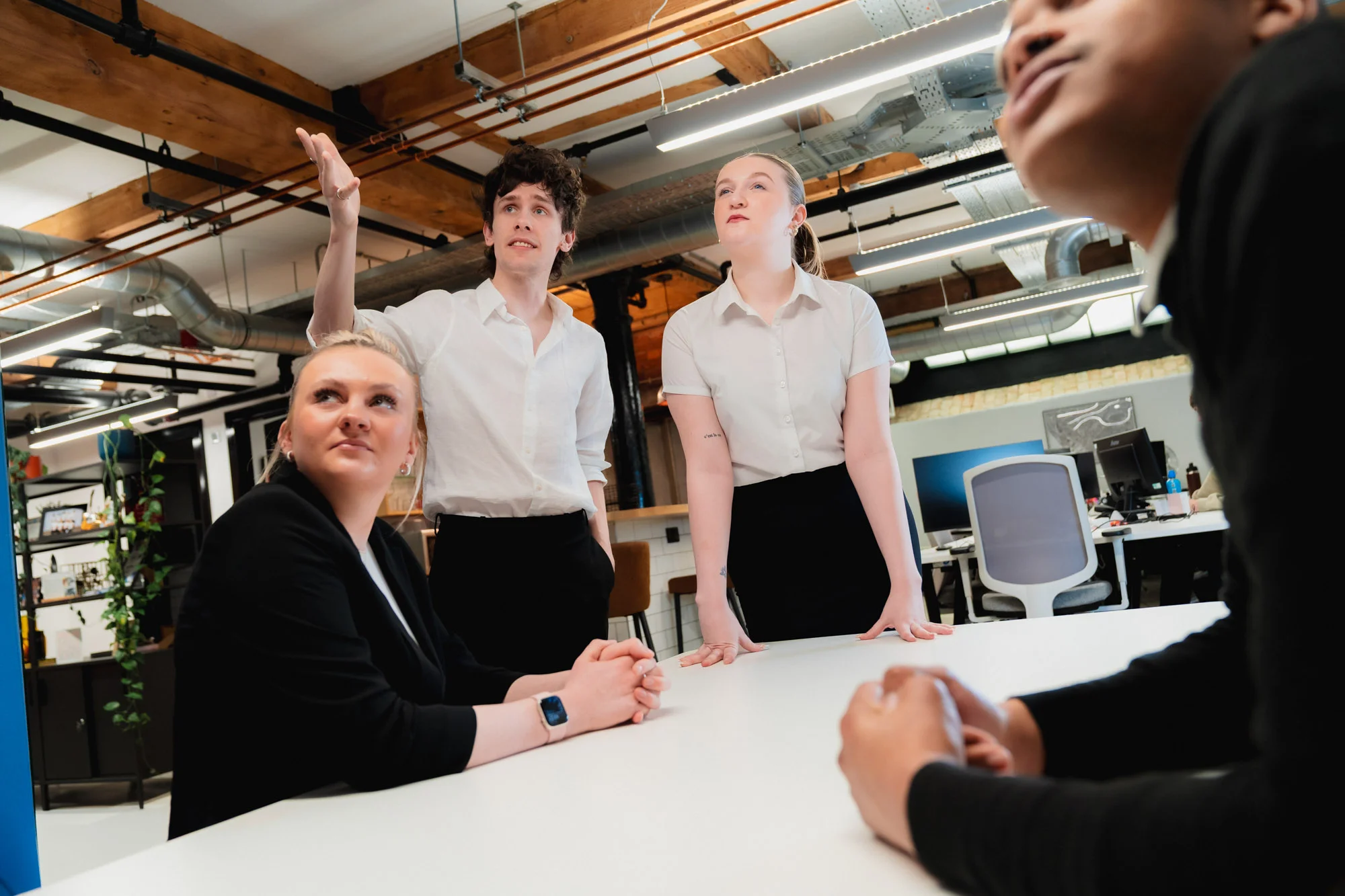 Group of people collaborating around a table in a modern office, with one person presenting ideas to the team.