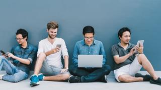 A group of four young people sat around using multiple devices