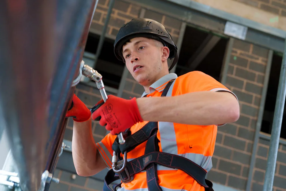 Person wearing a hard hat, high-visibility clothing and safety harness working on a construction site.