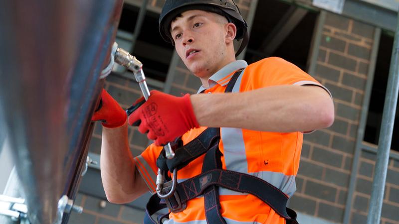 Person wearing a hard hat, high-visibility clothing and safety harness working on a construction site.