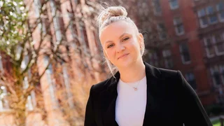 An image of a young professional outside. She's looking at the camera and smiling.