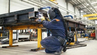 Worker welding metal beam in industrial workshop with protective equipment and sparks