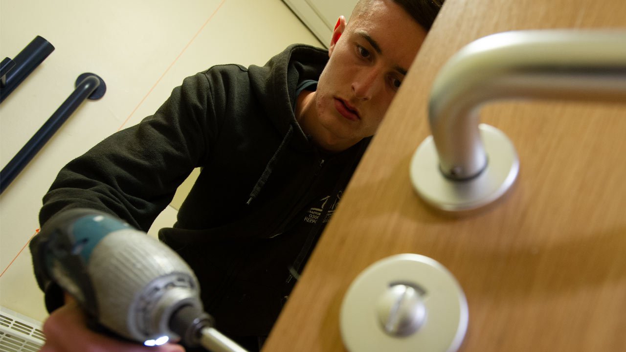 Tradesman with drill fixing a door handle.