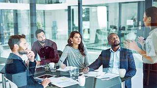 office workers sat at a desk and a woman standing talking to them