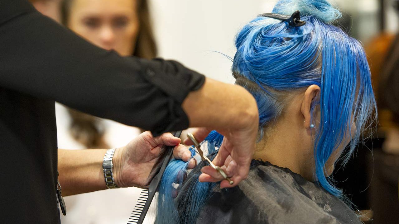 Hairdresser styles a client with blue hair.