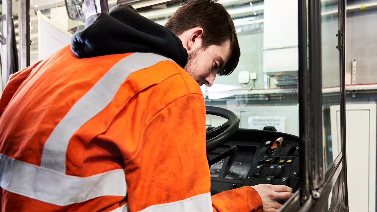 Over-the-shoulder view of an apprentice sat behind a steering wheel