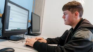 A side-on image of a young male learner sat at a computer in a classroom.